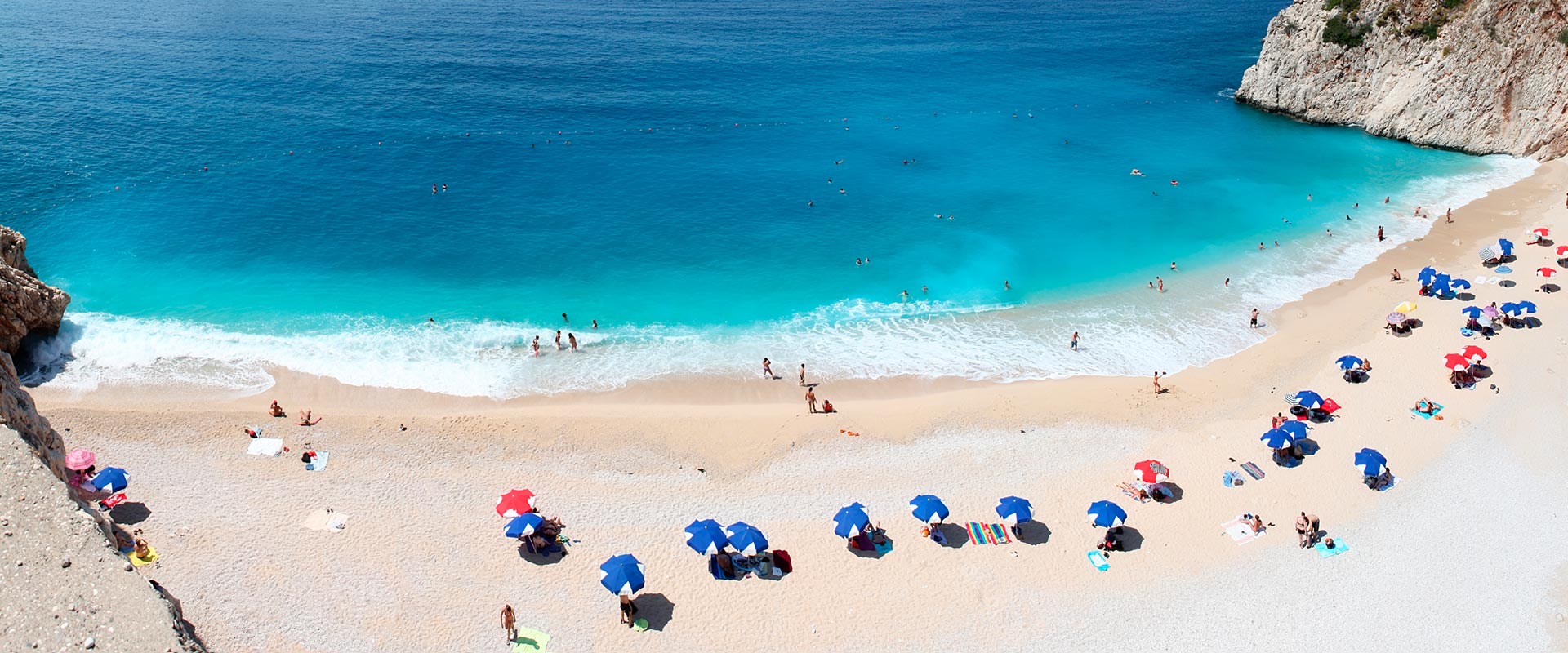 Panoramaansicht des Kaputaş-Strandes an der Türkischen Riviera, mit türkisfarbenem Wasser, Sandstrand und Klippen im Hintergrund.