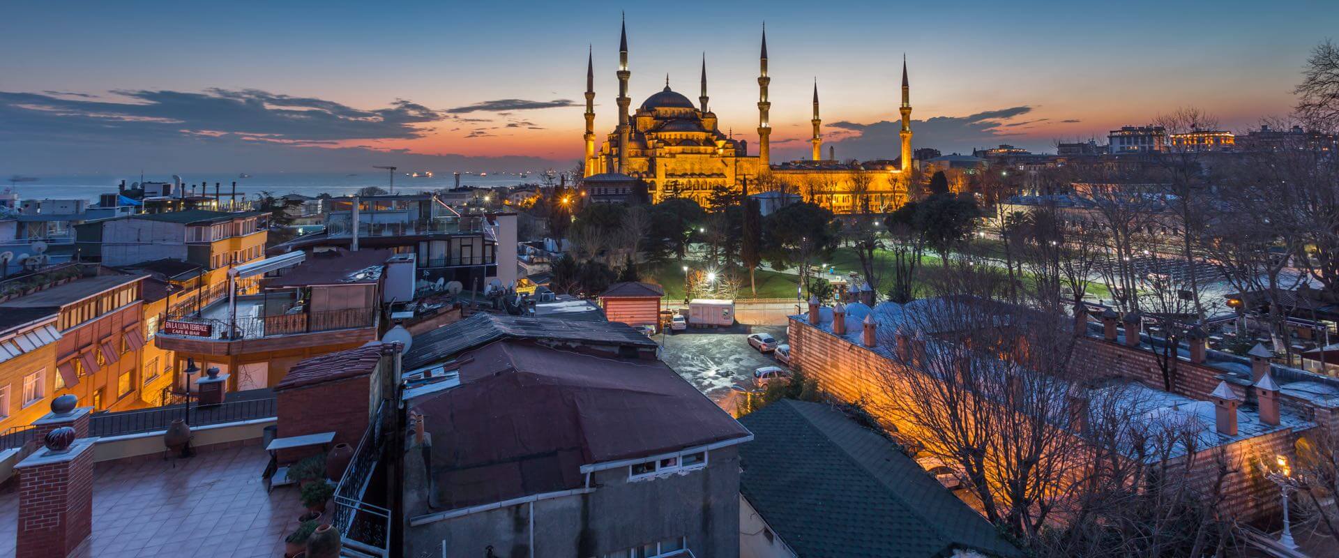 Panoramablick auf die Blaue Moschee bei Dämmerung in Istanbul, von einem Wohngebiet aus mit sichtbaren Dächern und Bäumen.