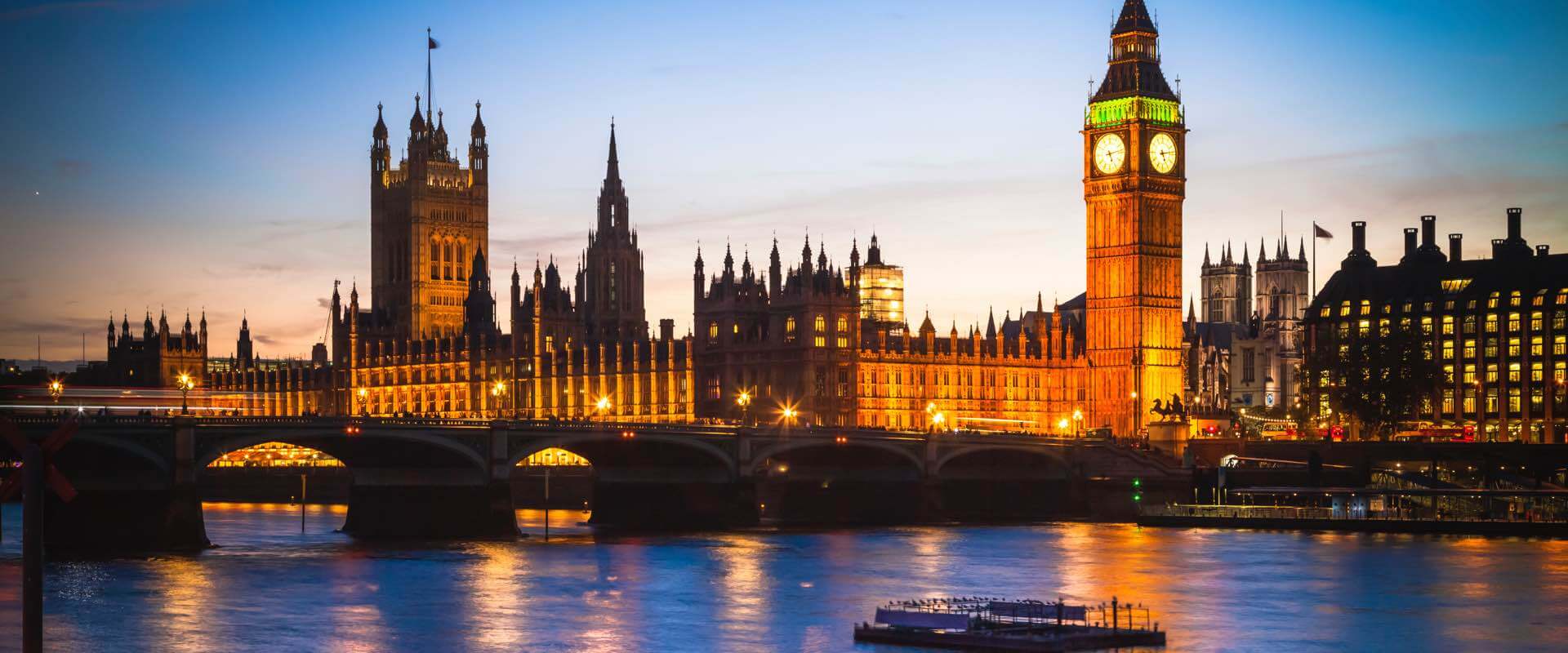 Nachtansicht des Palace of Westminster und Big Ben in London, mit der Themse, die das Stadtlicht widerspiegelt.